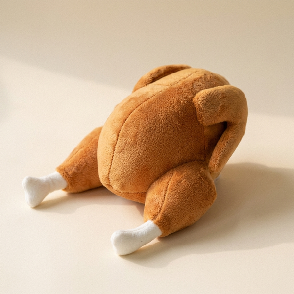 Squeaky roast chicken plush pet toy on cream studio background