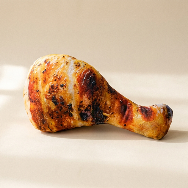 Realistic chicken leg plush squeaky dog toy on a cream studio background