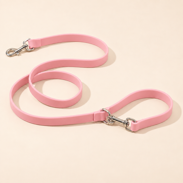 Silicone dog leash in pink with two silver swivel snap hooks, coiled on a cream background