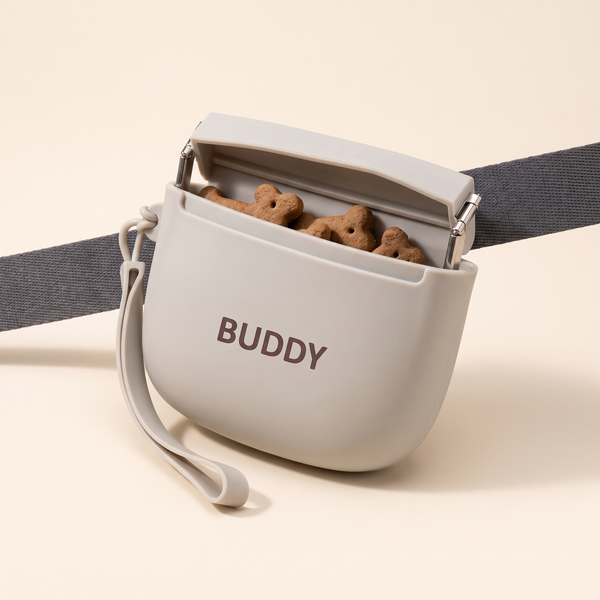 Personalized silicone dog treat bag in light gray printed with BUDDY, open with treats, on a gray strap
