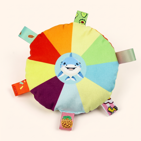Squeaky plush flying disc dog toy, shark design with rainbow panels and ribbon tabs, top view